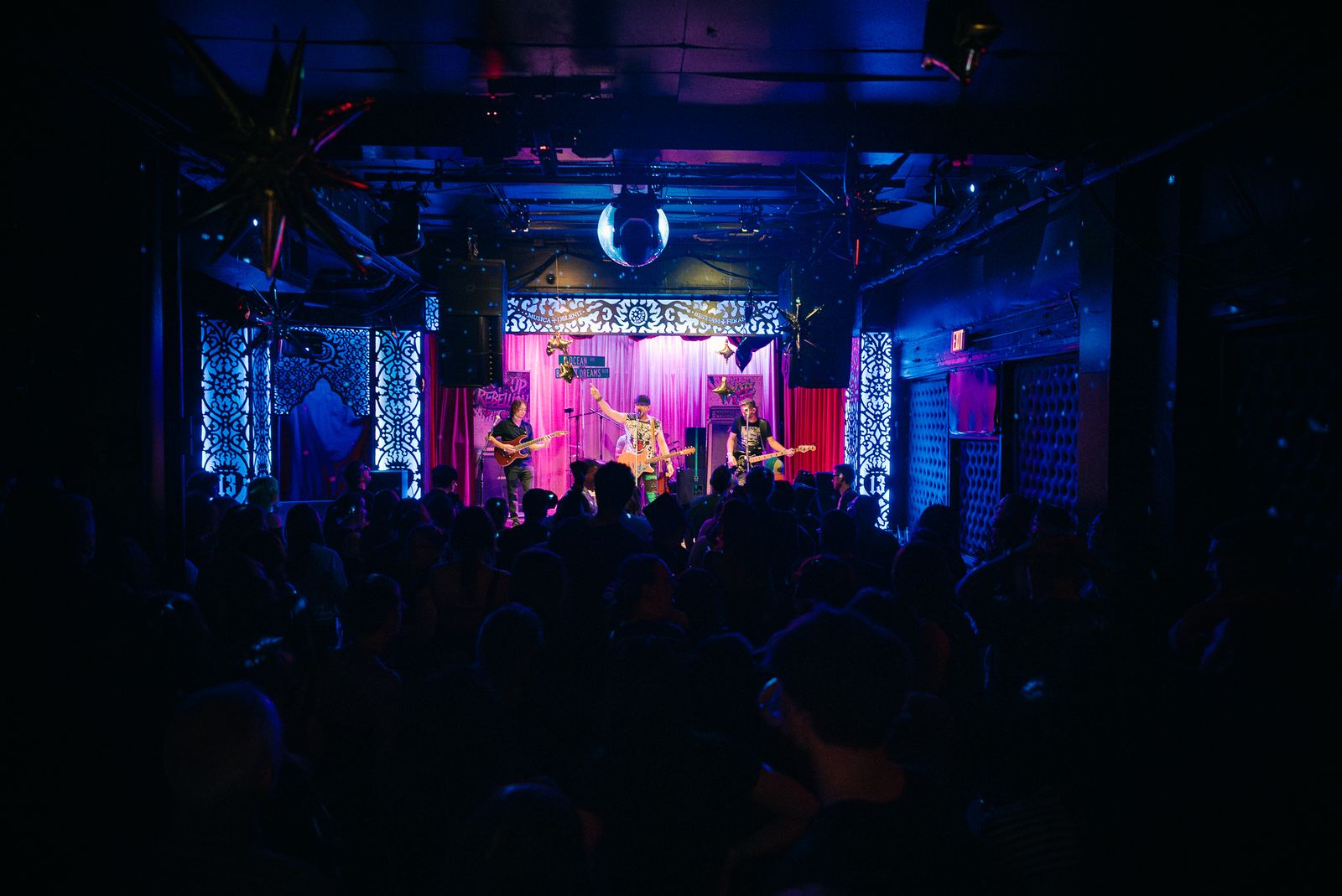 A packed club watching a band on a pink-lit stage under a mirror ball
