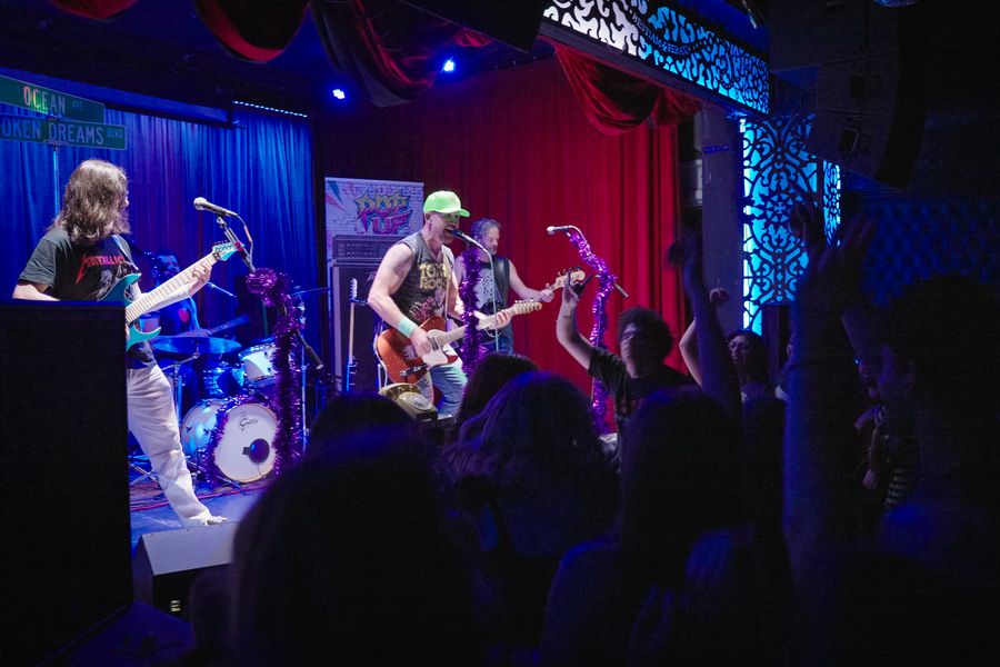 Fans with hands raised in front of a band on a red-curtained stage